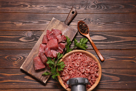 Manual meat grinder with beef mince, peppercorns and parsley on wooden table, flat layの写真素材