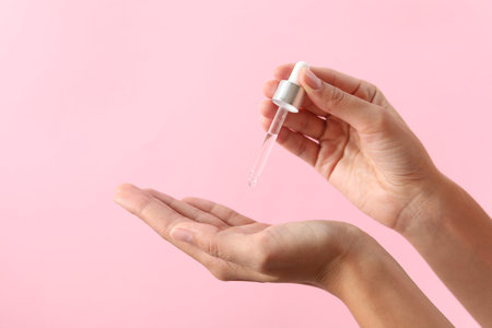 Woman applying cosmetic serum onto her hand on pink background, closeup. Space for textの写真素材