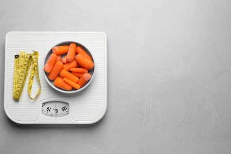 Healthy diet. Scale with carrots and measuring tape on light gray table, top view. Space for textの写真素材