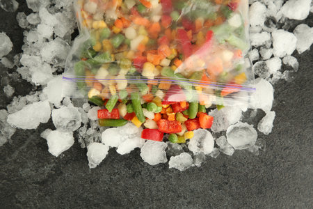 Zip bag with different frozen vegetables and ice on gray table, top viewの写真素材