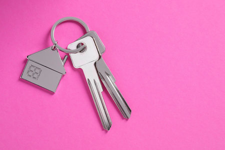 Keys with keychain in shape of house on pink background, top view. Space for textの写真素材