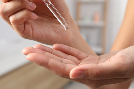 Woman applying cosmetic serum onto her hand on blurred background, closeupの写真素材