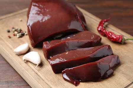 Cut raw beef liver with spices on wooden table, closeup