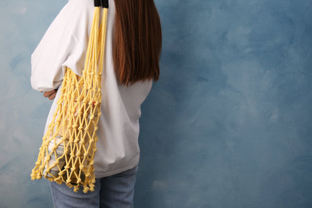 Woman with net bag full of different items near light blue wall, closeup and space for text. Conscious consumptionの写真素材