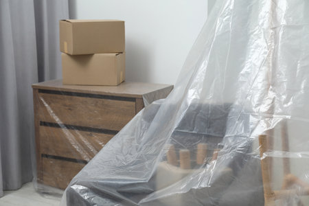 Modern furniture covered with plastic film and boxes at homeの写真素材