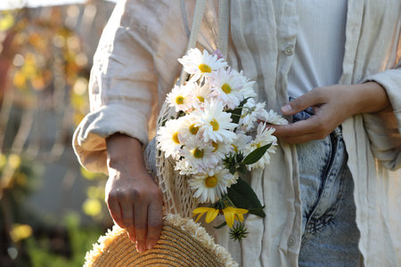 Woman holding net bag of beautiful white chamomile flowers outdoors, closeupの写真素材