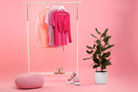 Rack with different stylish women`s clothes, sneakers and green plant on pink backgroundの写真素材