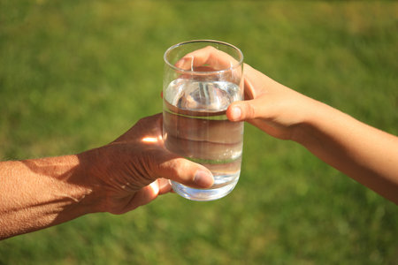Child giving glass of water to elderly woman outdoors on sunny day, closeupの写真素材