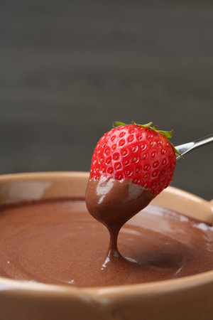 Strawberry with melted chocolate on fork above fondue, closeup. Space for textの写真素材