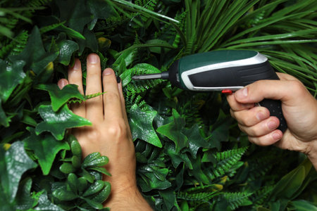 Man with screwdriver installing green artificial plant wall panel, closeupの写真素材