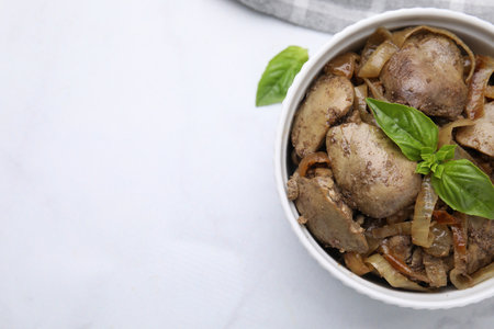 Delicious fried chicken liver with onion and basil in bowl on white table, top view. Space for textの写真素材