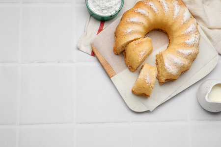 Delicious sponge cake served on white tiled table, flat lay. Space for text