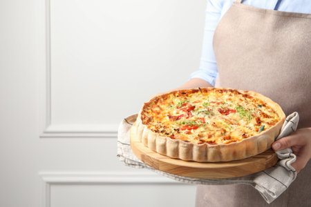 Woman holding board with tasty quiche indoors, closeup. Space for textの写真素材