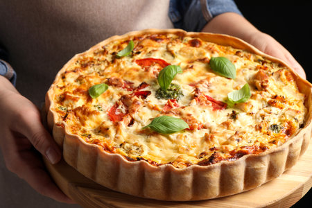 Woman holding board with tasty quiche on black background, closeupの写真素材
