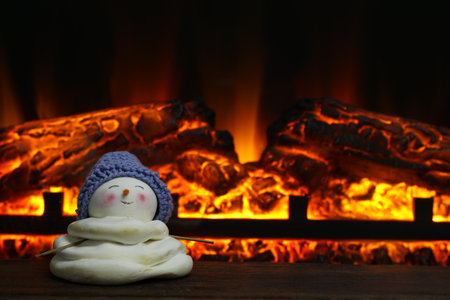 Cute decorative snowman in hat on wooden floor near fireplace, space for textの写真素材