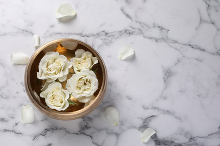 Tibetan singing bowl with water and beautiful roses on white marble table, top view. Space for textの写真素材
