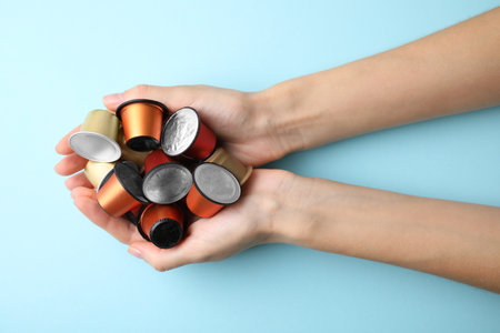 Woman holding heap of coffee capsules on light blue background, top viewの写真素材