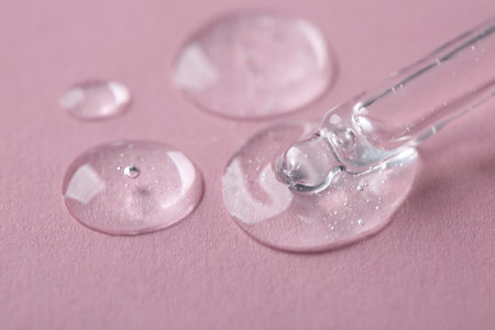 Dripping cosmetic serum from pipette onto pink background, macro viewの写真素材