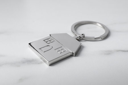 Metal keychain in shape of house on marble table, closeup