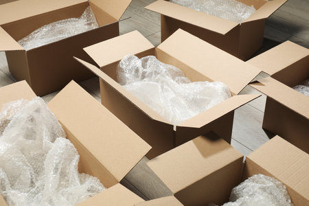 Many open cardboard boxes with pooping wrap on white wooden floor