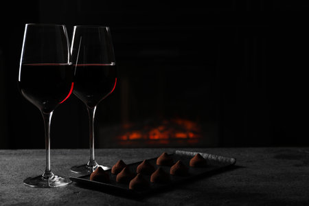 Glasses of red wine and chocolate truffles on gray table in darkness, space for textの写真素材