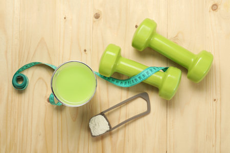 Tasty shake, dumbbells, measuring tape and powder on wooden table, flat lay. Weight lossの写真素材