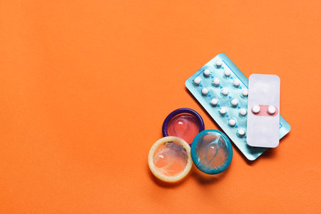 Condoms and birth control pills on orange background, flat lay and space for text. Choosing method...