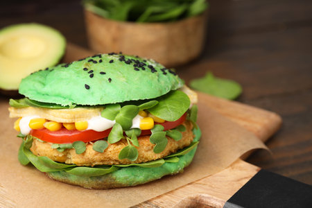 Tasty green vegan burger with vegetables, patty and microgreens on wooden table, closeup. Space for textの写真素材