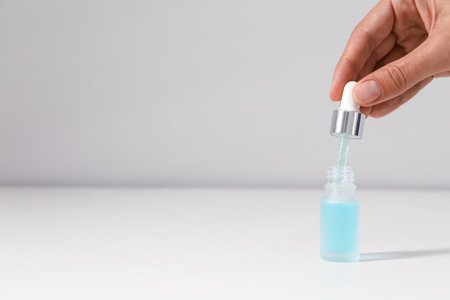 Woman with cosmetic serum at white table, closeup. Space for textの写真素材