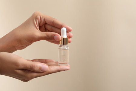 Woman with bottle of cosmetic serum on beige background, closeup. Space for textの写真素材
