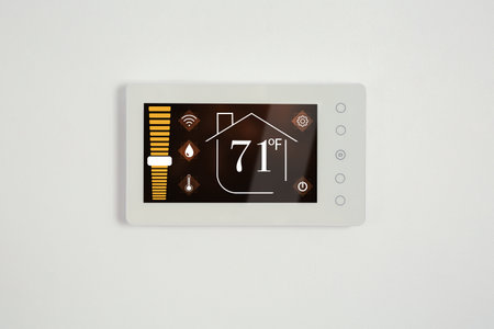 Thermostat displaying temperature in Fahrenheit scale and different icons. Smart home device on white wallの写真素材