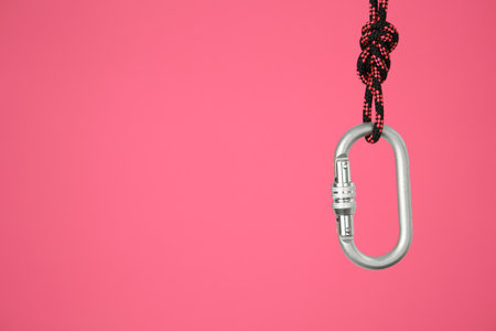 One metal carabiner hanging on rope against bright pink background. Space for textの写真素材