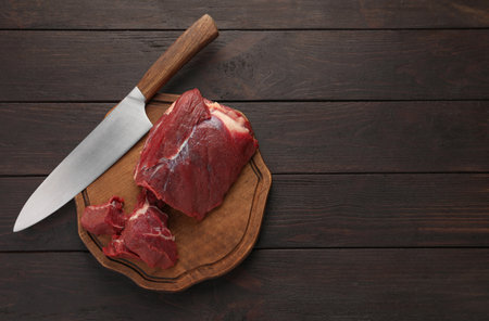 Pieces of raw beef meat and knife on wooden table, top view. Space for textの写真素材