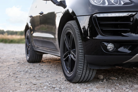 Modern black car parked on rubble road outdoors