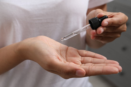 Woman applying cosmetic serum onto her hand on blurred background, closeupの写真素材