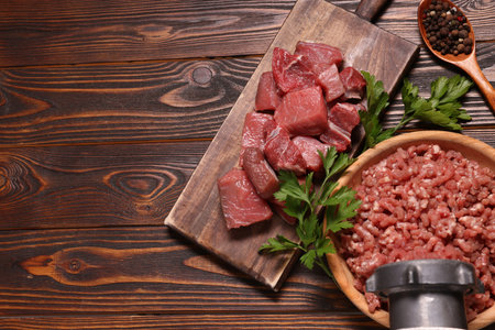 Manual meat grinder with beef, peppercorns and parsley on wooden table, above view. Space for text