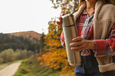 Woman with metallic thermos outdoors, closeup. Space for textの写真素材