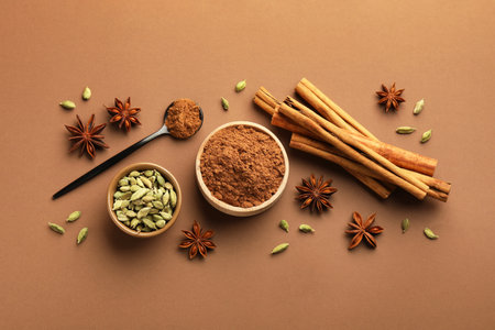 Cinnamon sticks, powder, star anise and cardamom pods on brown background, flat layの写真素材