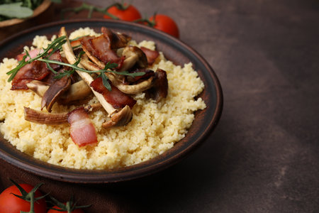 Tasty couscous with mushrooms and bacon in bowl on brown table, closeup. Space for textの写真素材