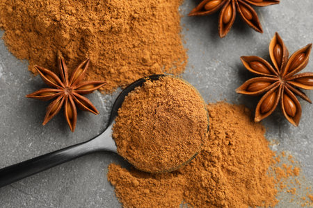 Spoon with cinnamon powder and star anise on gray table, flat lay