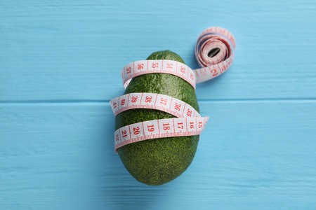 Healthy diet. Avocado and measuring tape on light blue wooden table, top viewの写真素材