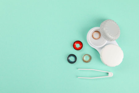 Different color contact lenses, tweeters and case on turquoise background, flat lay. Space for textの写真素材