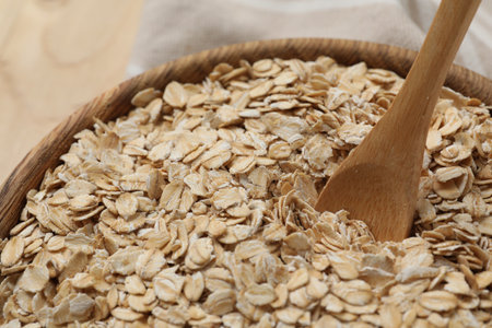 Wooden bowl and spoon with oatmeal on table, closeup