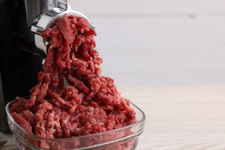 Electric meat grinder with beef mince on table, closeup. Space for text