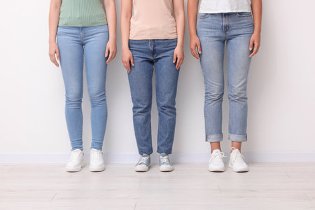 Women in stylish jeans near white wall, closeup