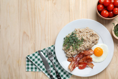 Delicious boiled oatmeal with fried egg, bacon and tomato served on wooden table, flat lay. Space for textの写真素材