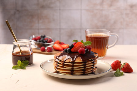 Stack of tasty pancakes with fresh berries, chocolate sauce and mint on white table