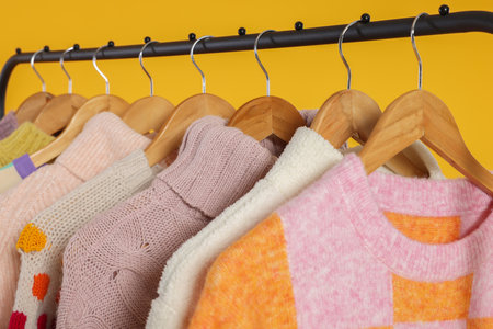 Rack with stylish women's sweaters on wooden hangers against orange background, closeupの写真素材
