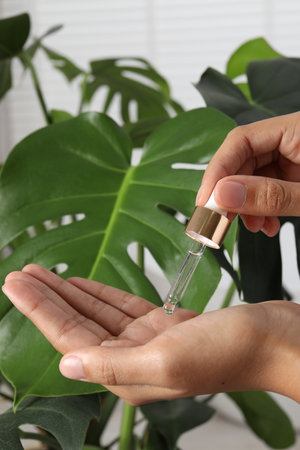 Woman applying cosmetic serum onto her hand near green plant, closeupの写真素材