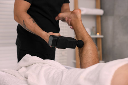 Man receiving professional leg massage with electric gun in spa salon, closeupの写真素材
